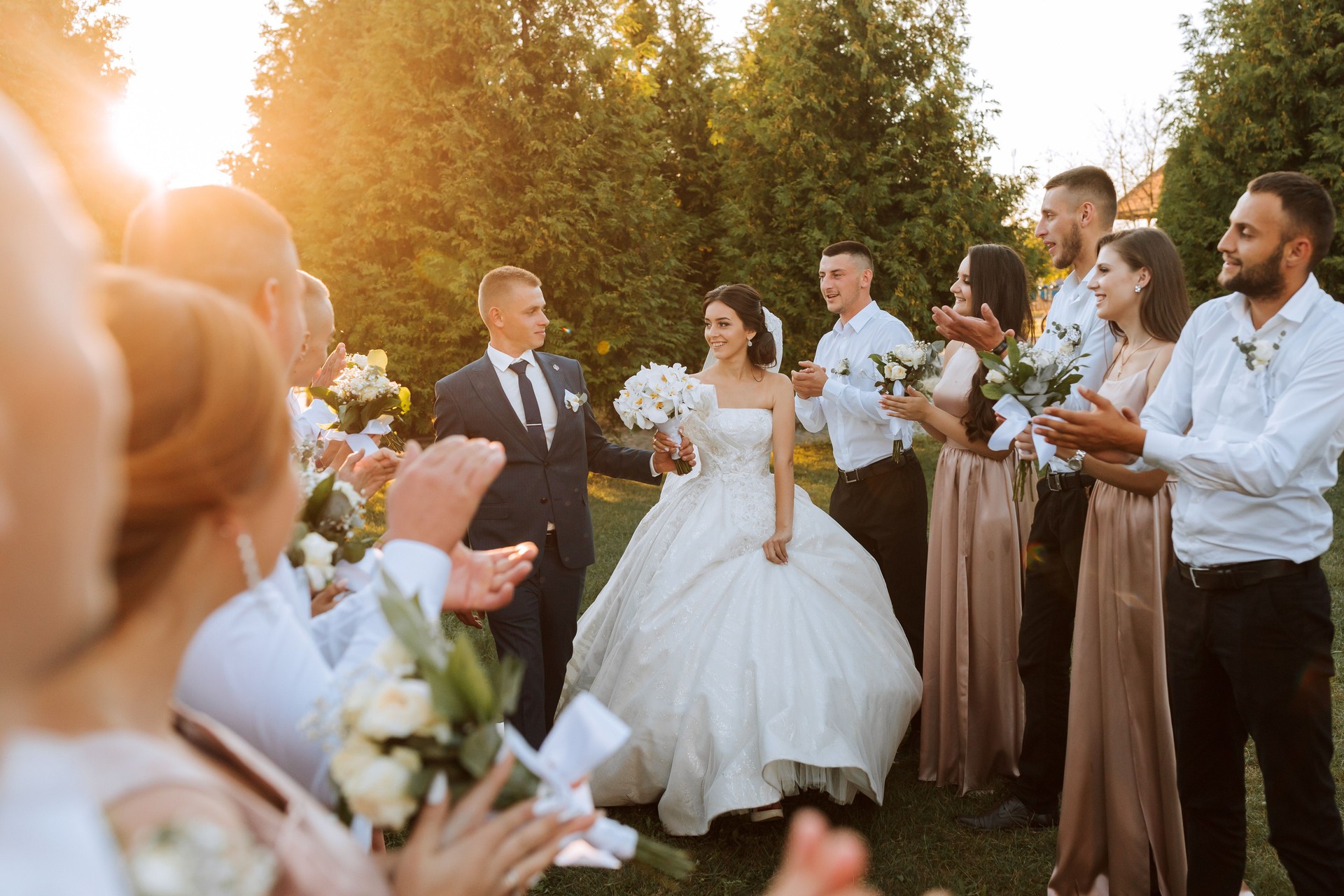 Wide angle shot of bride and groom walking down the aisle after their wedding ceremony at sunset as friends and family celebrate